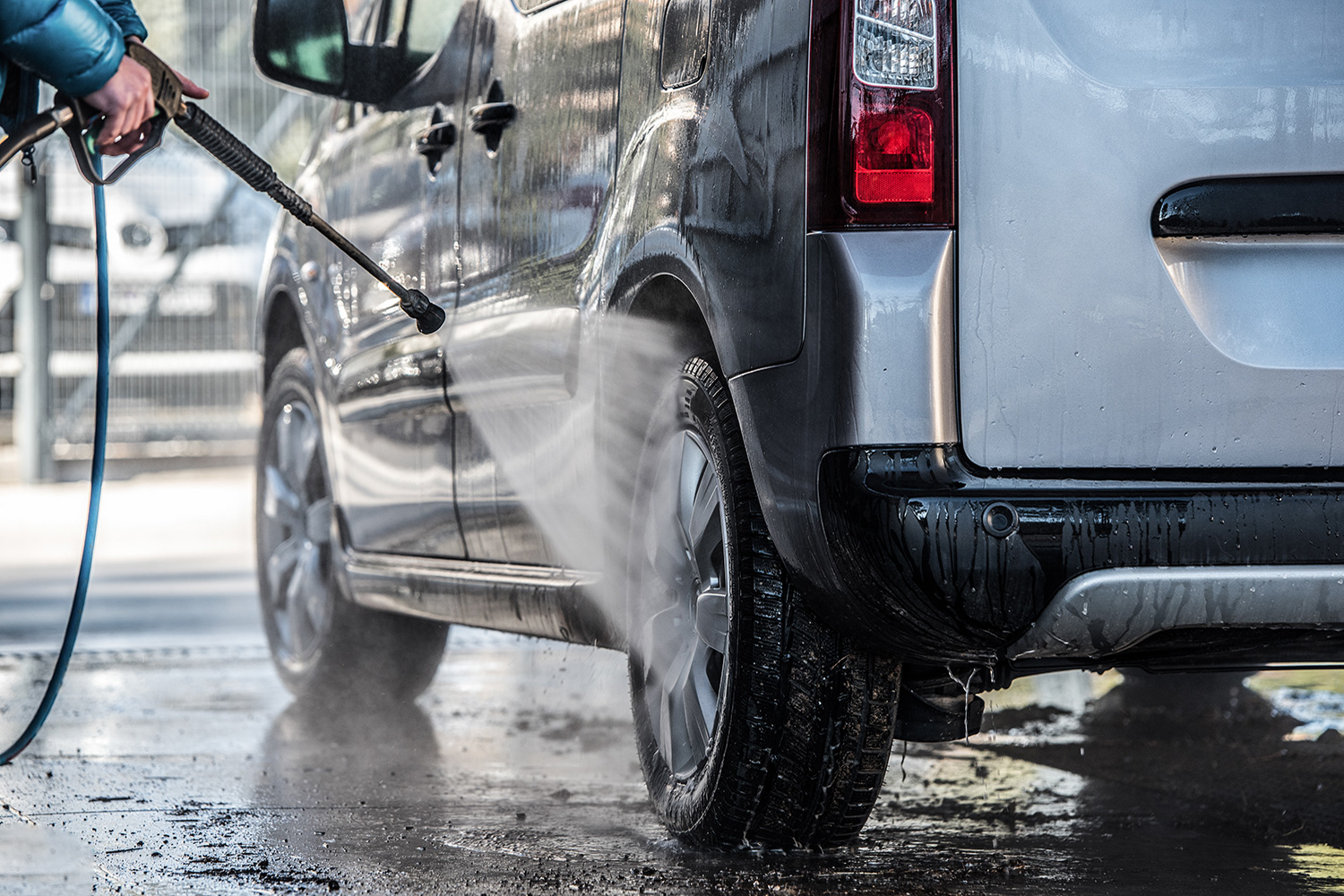 Der Reifen von einem Auto wird mit einem Wasser-Schlauch abgespritzt